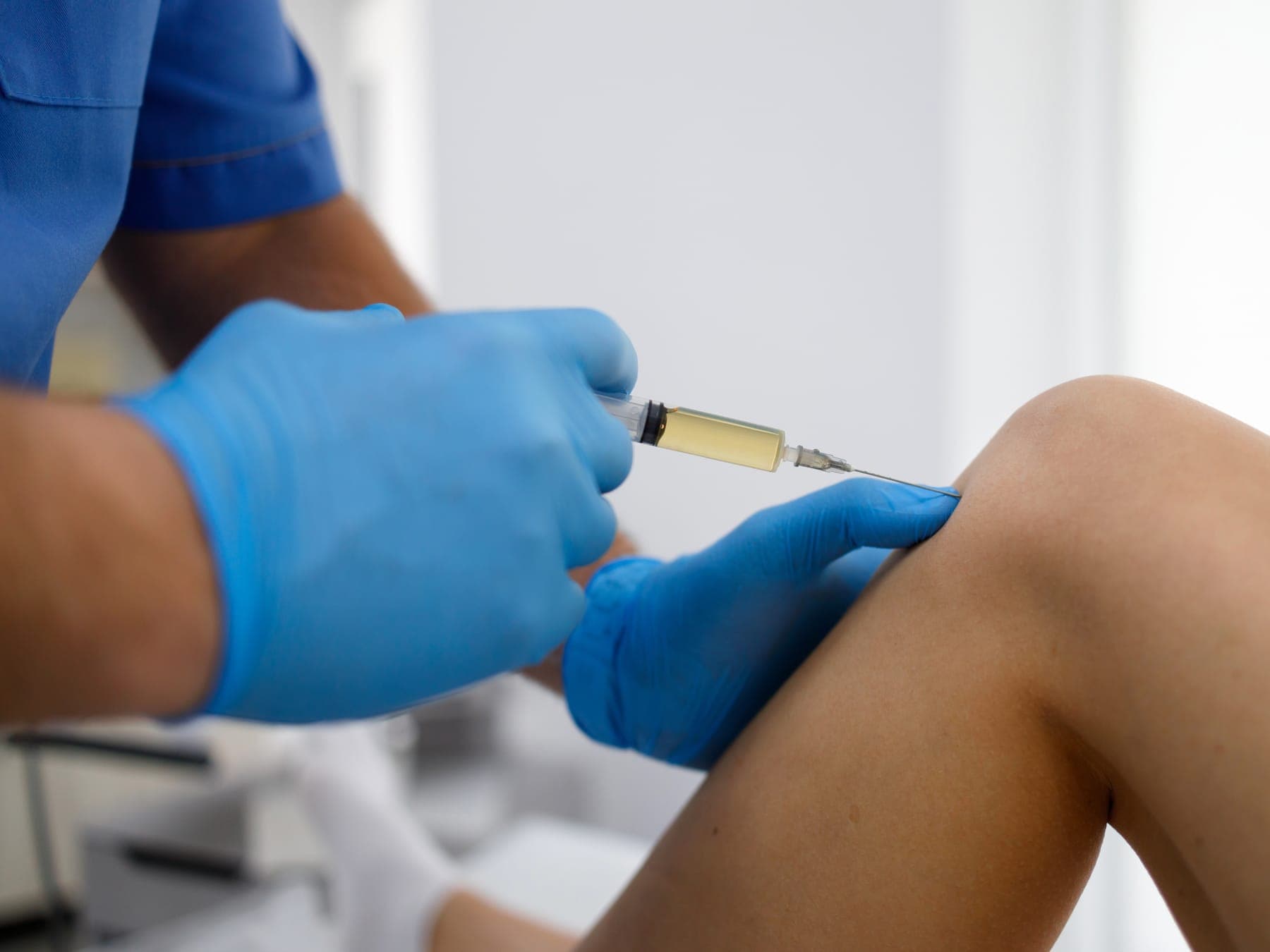 Médico infiltrando la rodilla de un paciente con guantes estériles