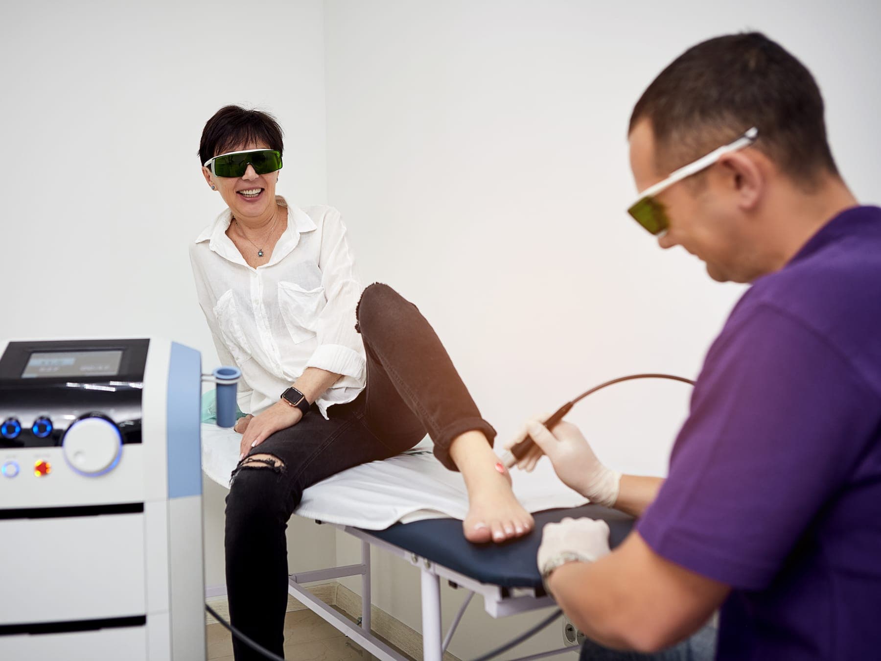 Kinesiólogo aplicando láser terapia en el pie de una paciente, ambos con lentes de protección