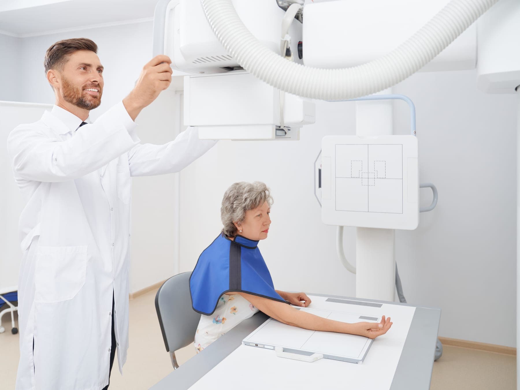 Radiólogo ajustando el equipo para tomar una radiografía a una paciente con delantal plomado
